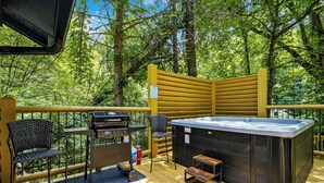 Eine Terrasse mit Whirlpool, Grill und Sitzbereich, umgeben von Bäumen.