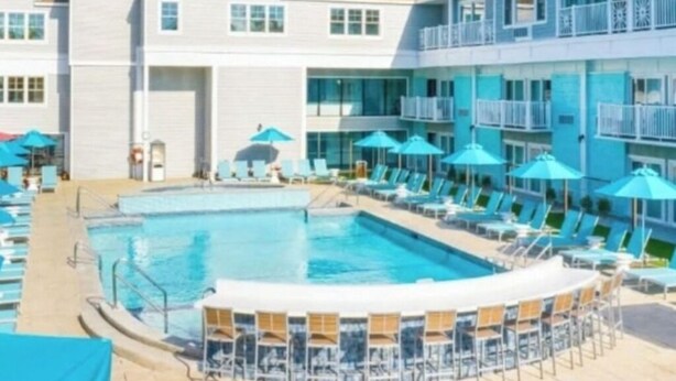 Un espace piscine doté de chaises longues et de parasols, entouré d’immeubles à plusieurs étages avec des balcons.