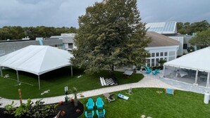 Une cour avec un grand arbre, des sièges en plein air et une tente blanche.