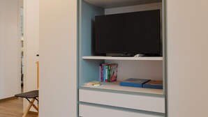 A room with a television on a shelf, a chair, and books on another shelf. - [Prima Classe Apartment] Central Cozy Apartment (Molfetta)