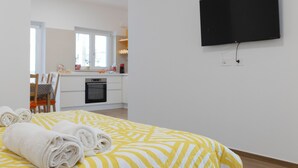 A hotel room with a bed, a TV mounted on the wall, and a kitchen area visible through an open door. - [Prima Classe Apartment] Central Cozy Apartment (Molfetta)