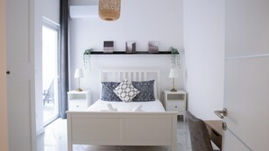 Une chambre moderne comprenant un lit, des tables de chevet, un luminaire suspendu, une fenêtre et une étagère murale agrémentée d’objets décoratifs.