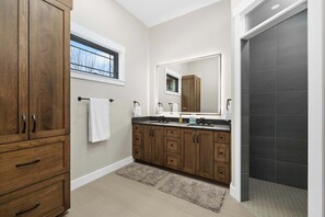 A bathroom with wooden cabinets, a large mirror, a window, and a shower area.