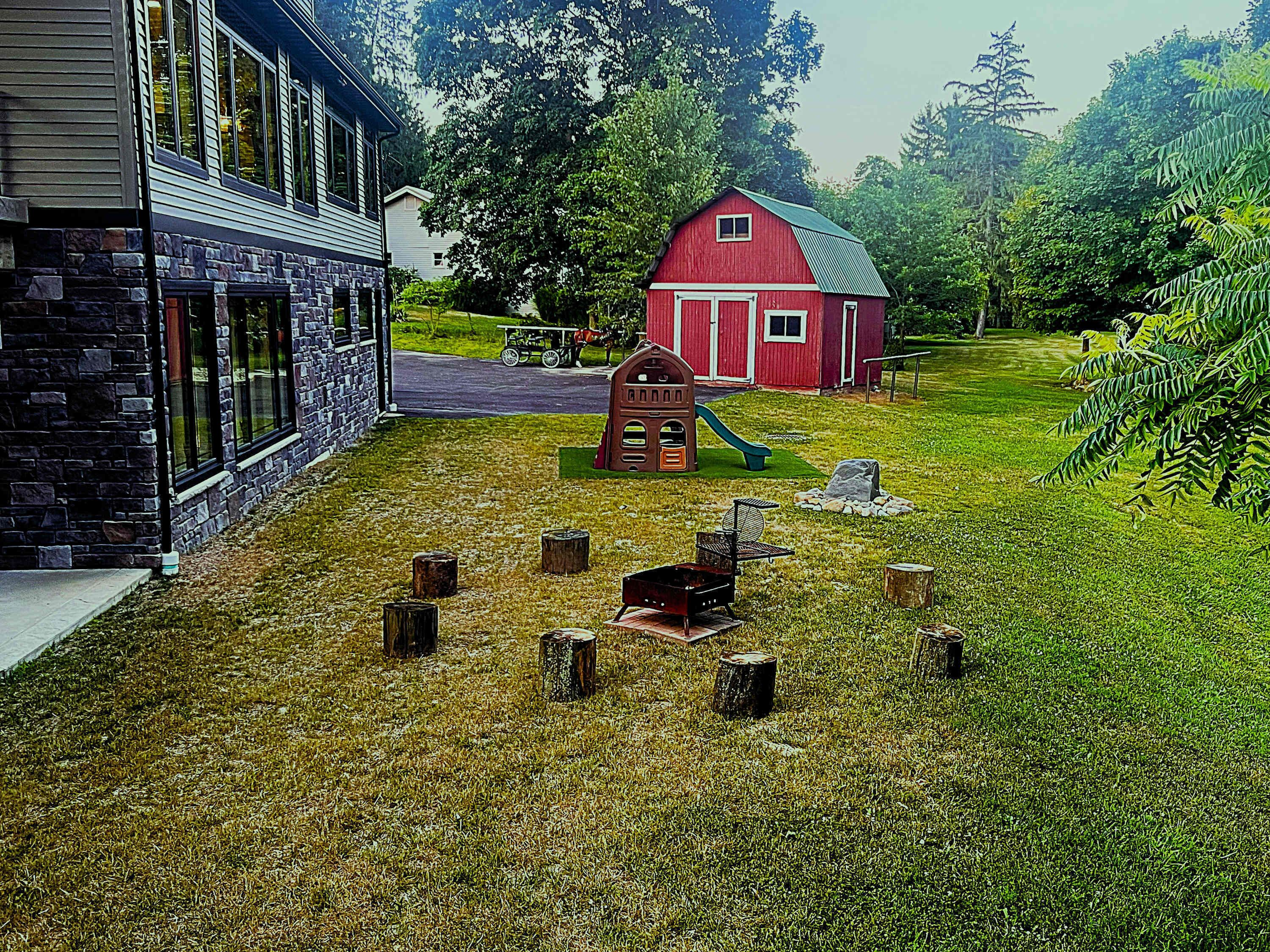 A house with a stone facade, a red barn, and a grassy yard with a swing set.