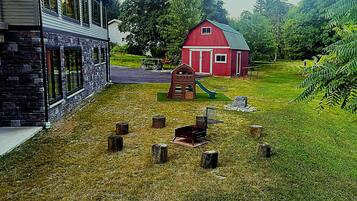A house with a stone facade, a red barn, and a grassy yard with a swing set.