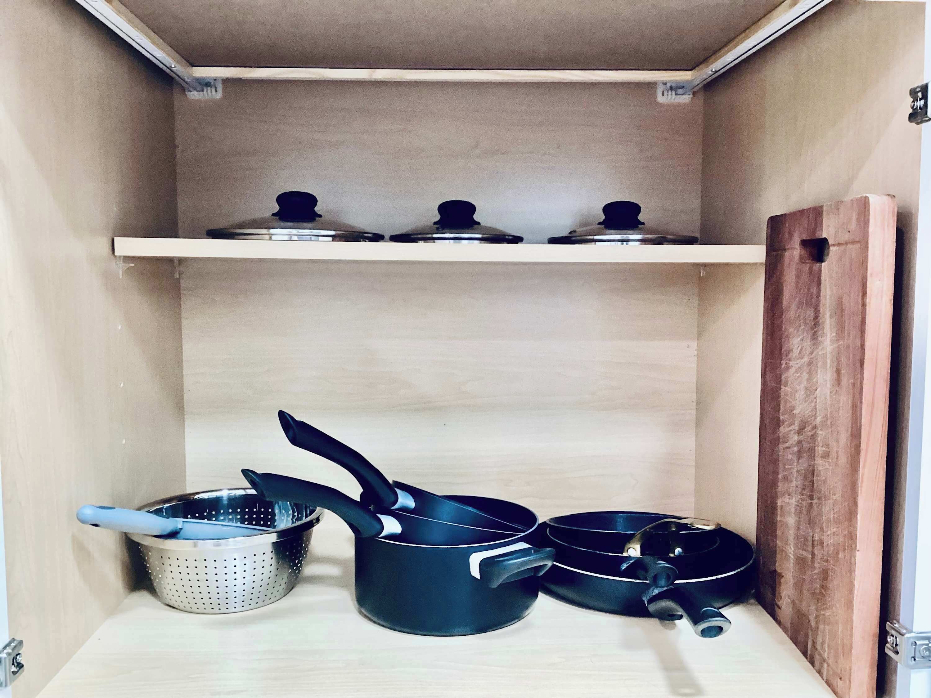 Een keuken met een houten plank waarop drie pannen en een vergiet staan.