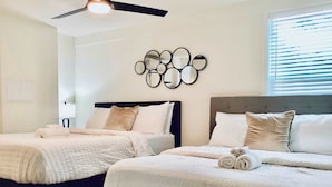 A hotel room with two beds, a ceiling fan, a wall-mounted mirror, and a window with blinds. - Boardwalk Bungalow 1 For 6 (League City)