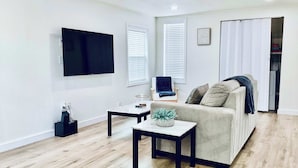 A modern living room with a flat-screen TV, a sofa, a coffee table, and a chair. - Boardwalk Bungalow 1 For 6 (League City)