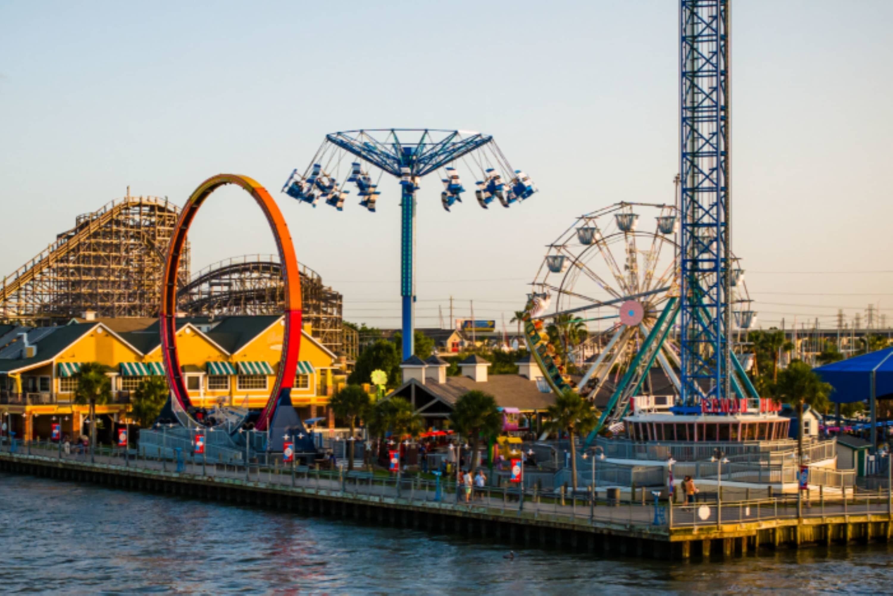 A waterfront amusement park with various rides and a Ferris wheel.