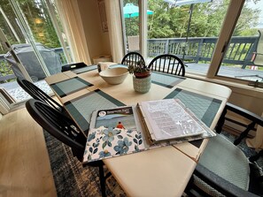 A dining area with a table set for two, a bowl, a potted plant, and a book titled 'Damariscotta Region 2023 Guide'. - Pemaquid Trail Gem: Water Views + Huge Deck + Private Beach Access (Bristol)