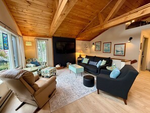 Una sala acogedora con techo de madera, chimenea, sofá, sillón y mesa de centro.