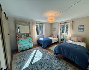 A bedroom with two beds, a dresser, a mirror, and a window with curtains.
