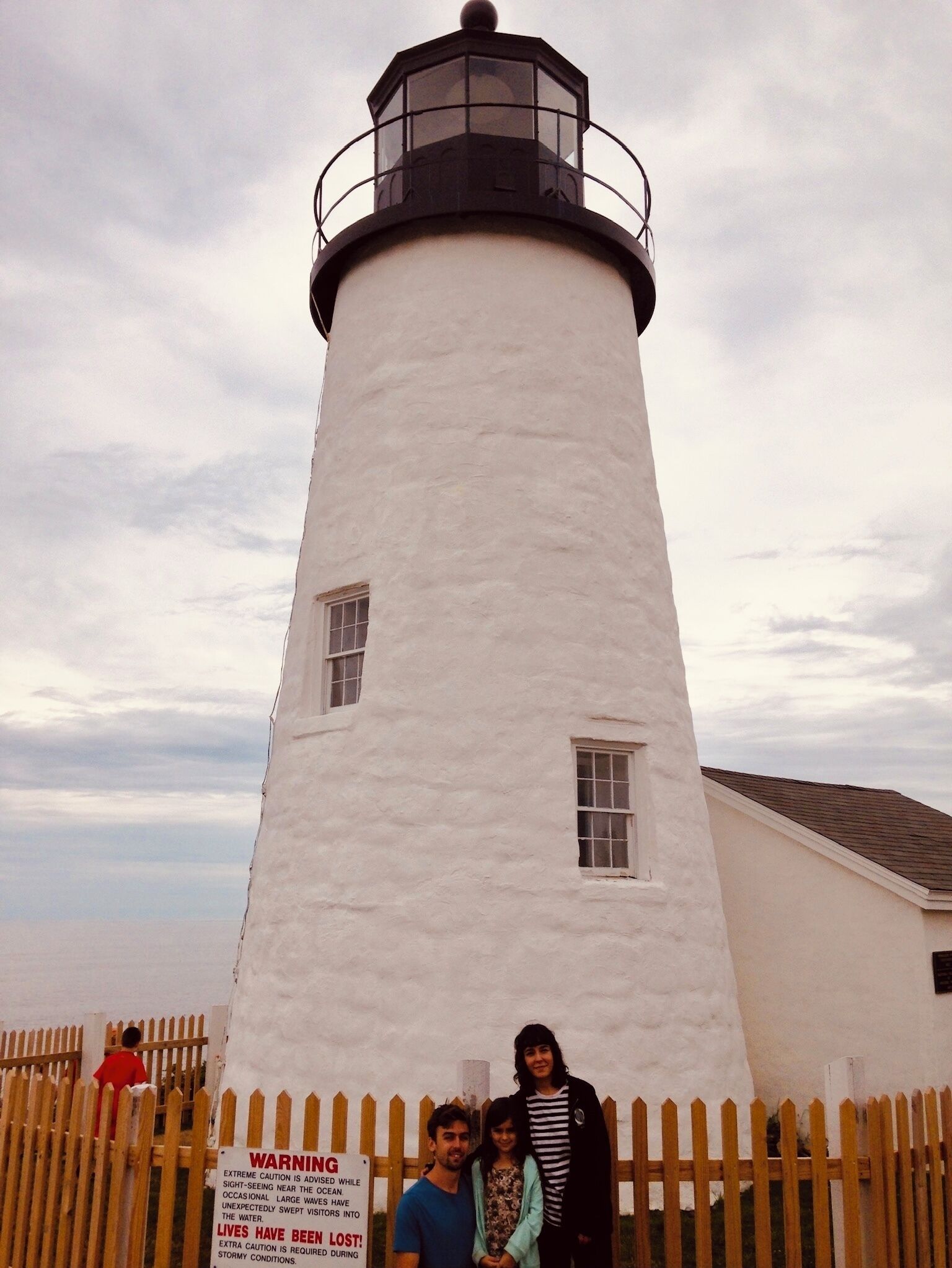 A white lighthouse with a black top and a warning sign about ocean dangers.