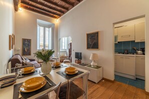 A dining area with a table set for four, a sofa, a TV, and a kitchen visible in the background. - Minerva 5 - FromeHometoRome (Roma)