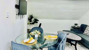 Ett modernt vardagsrum med ett matbord i glas, blå stolar, en grå soffa och en platt-TV som är monterad på väggen.