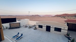 A rooftop terrace with lounge chairs, a small seating area, and a view of a desert landscape.