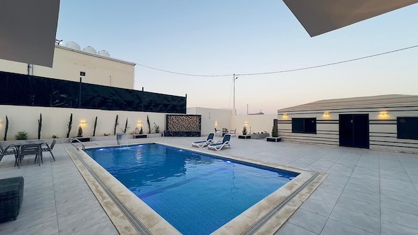 A rooftop pool area with lounge chairs, a small table, and a decorative wall.