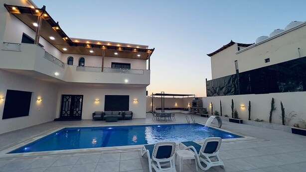 Uma área de piscina moderna com piscina retangular, espreguiçadeiras e um espaço de estar coberto.