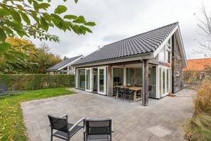 Una casa moderna con tetto spiovente, ampie vetrate e un patio arredato con mobili da esterno.