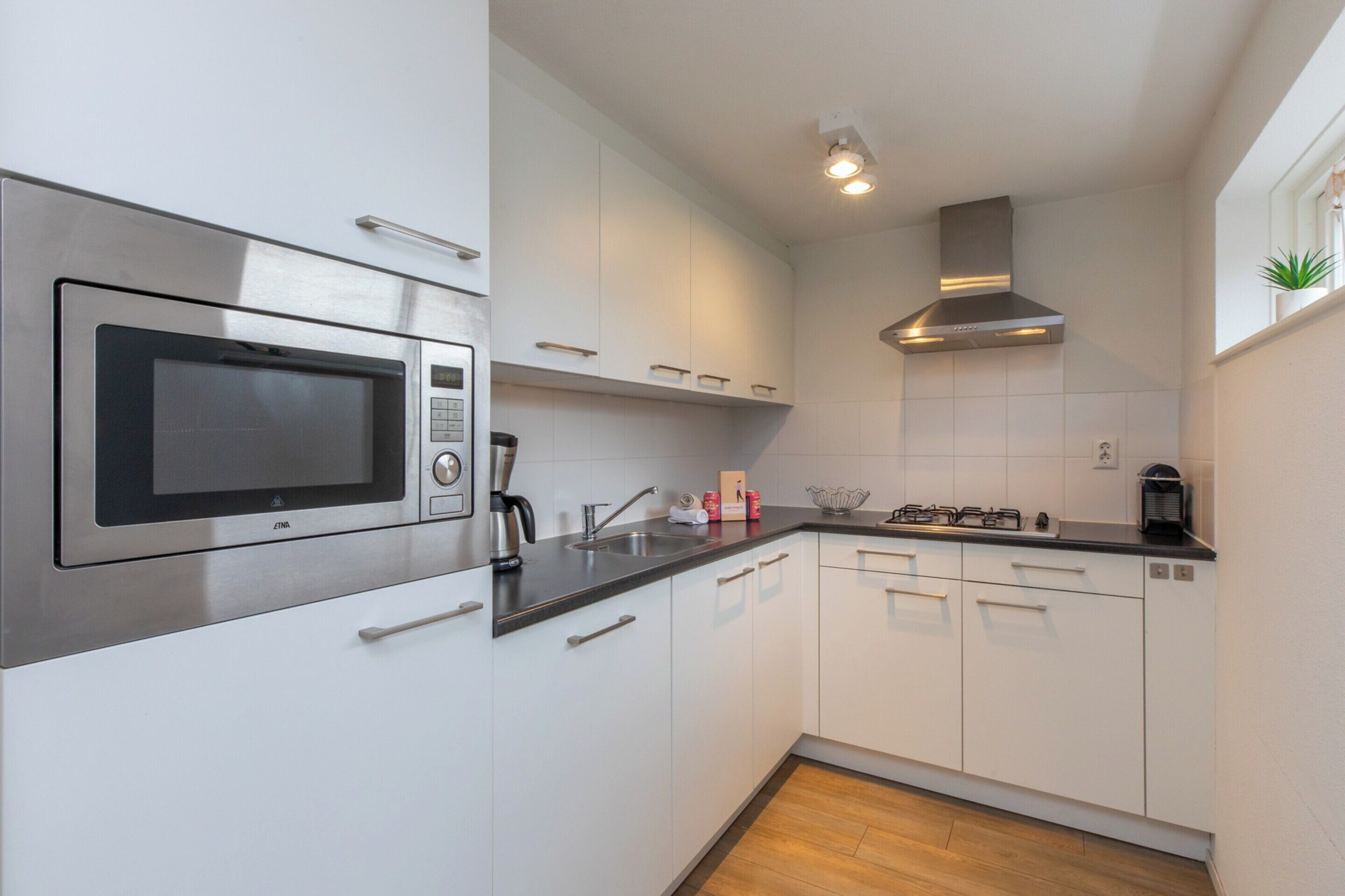 A modern kitchen with white cabinets, a stainless steel microwave, a gas stove, and a built-in oven.