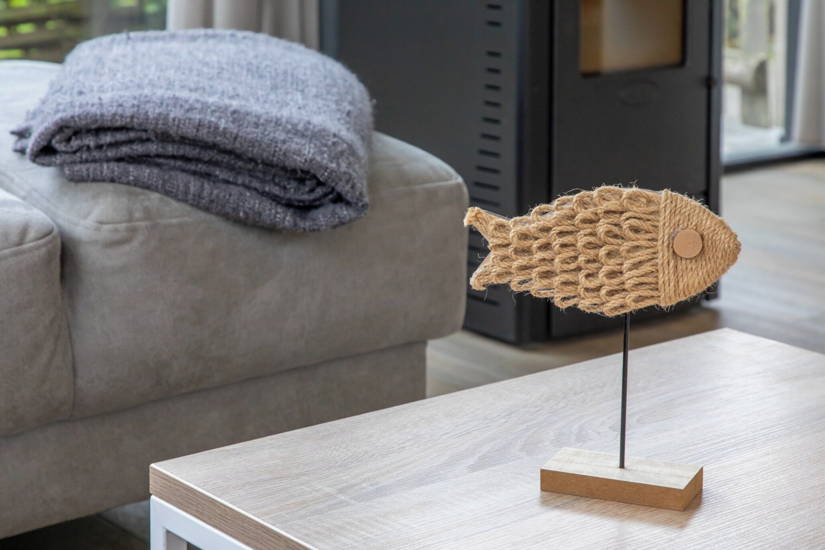 A fish-shaped sculpture on a wooden stand in a living room with a grey couch and a grey blanket in the background.