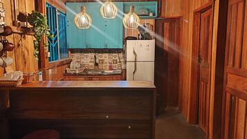 A wooden interior with a kitchen area featuring a blue backsplash, a refrigerator, and hanging pendant lights.