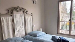 Quarto com duas camas, uma janela e luminária fixada na parede.