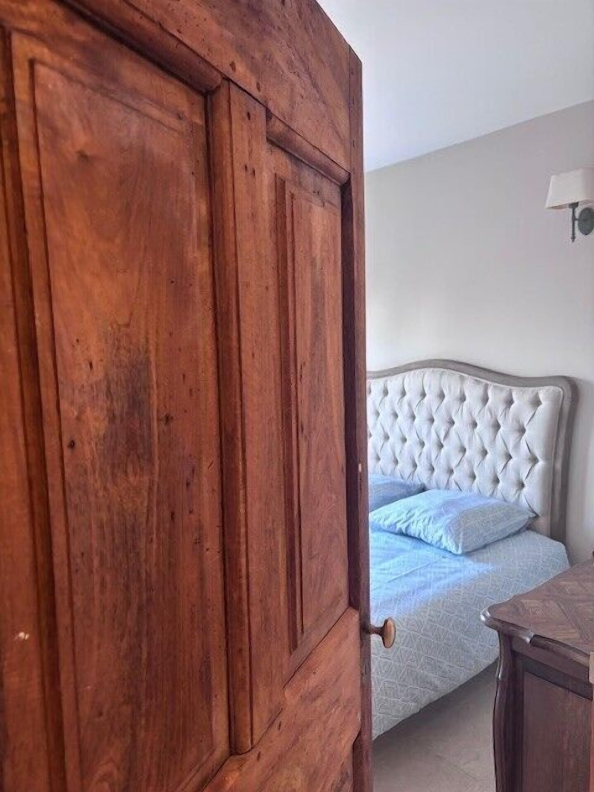 Une chambre avec une porte en bois, un lit doté d’une tête de lit capitonnée et une table de chevet.