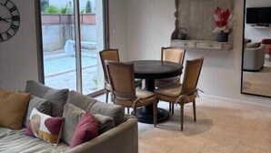 Uma sala de estar com sofá, mesa de jantar, cadeiras, relógio e televisão.