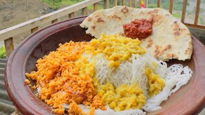 Un piatto di cibo con riso, uova e pane piatto, sorretto sopra una ringhiera con vista su un paesaggio montuoso.