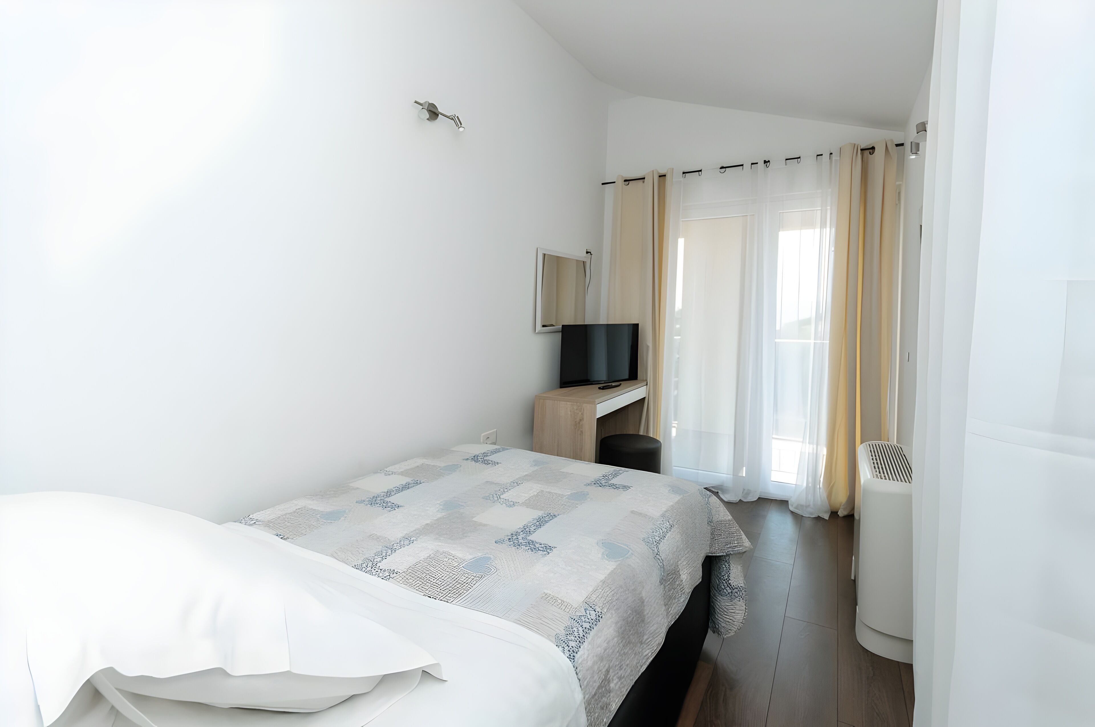 Ein Hotelzimmer mit Bett, Schreibtisch, Fernseher und einem Fenster mit Vorhängen.