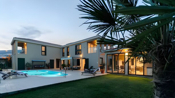 Ein modernes, zweistöckiges Haus mit Schwimmbad, Außenbereich zum Sitzen und einem gepflegten Rasen.