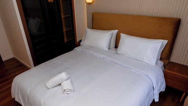 A neatly made bed with white linens and a rolled towel, a wooden headboard, a bedside table, and a hanging light fixture. - Votre Appart Cosy avec 2 terasses Calmes (Casablanca)