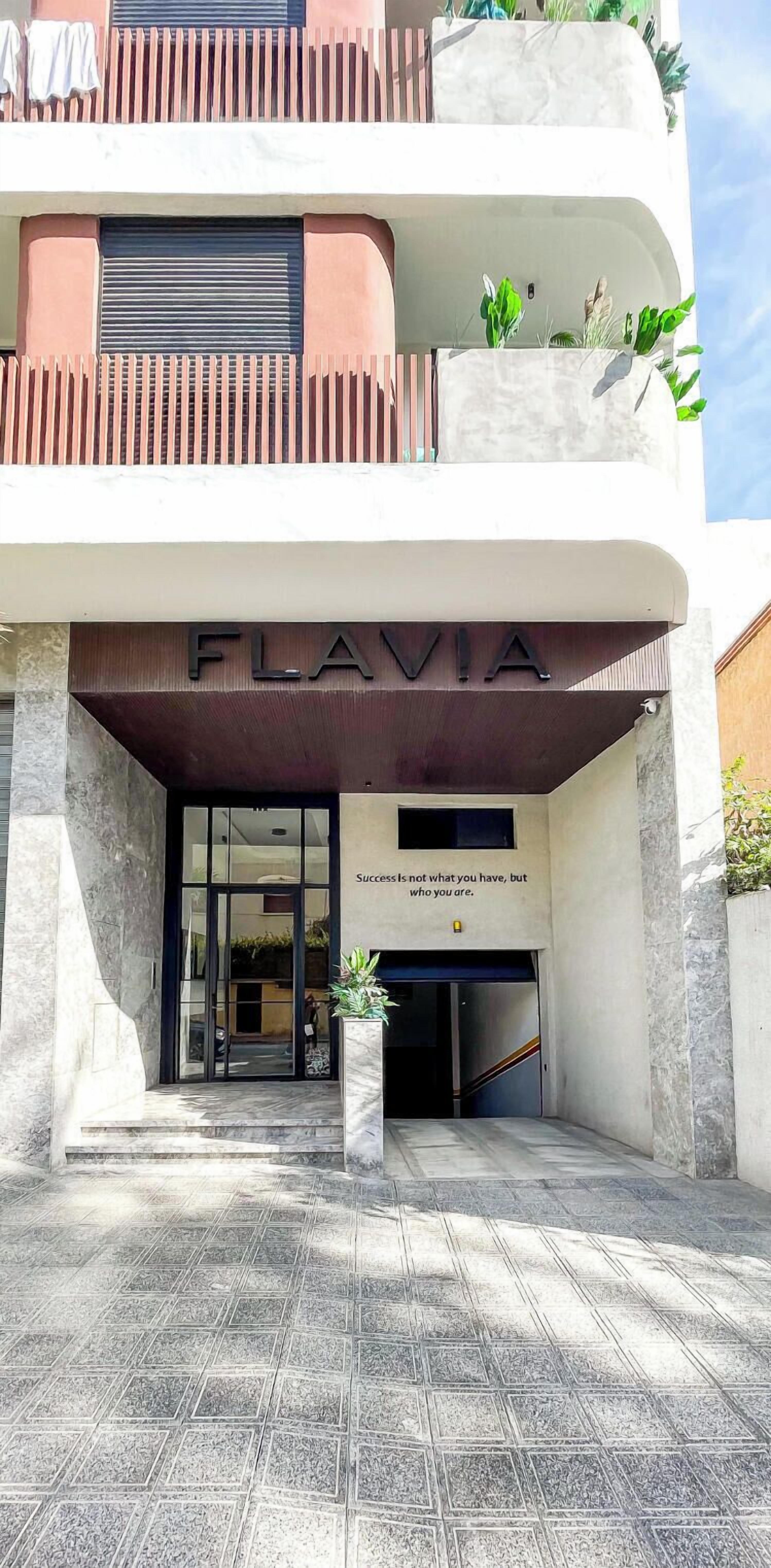 Un edificio con un cartel que dice "FLAVIA" y una cita debajo.