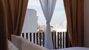 Habitación de hotel con cama, cortinas blancas y vistas a edificios a través del ventanal.