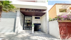 La entrada a un edificio llamado FLAVIA, con una cita en la pared y una planta en maceta al frente.