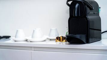A kitchen counter with a coffee machine, three white cups, and two gold capsules.