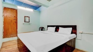 A single bed in a room with a wooden floor, a wooden door, and a light blue wall. - Shree Radhe Krishna Guest House (Jhansi)