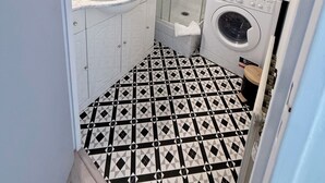 Ett litet badrum med handfat, spegel, dusch och tvättmaskin.