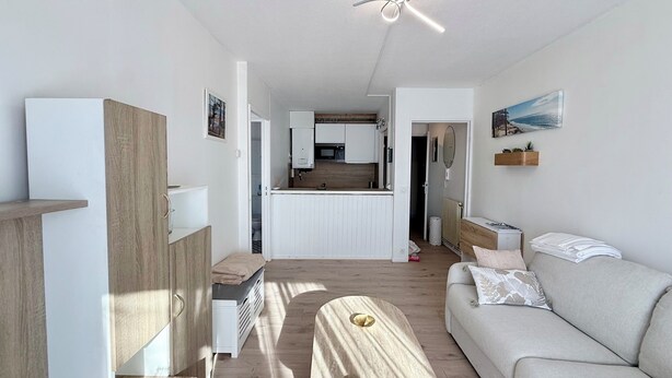 Ett modernt och väl upplyst vardagsrum med en soffa, ett soffbord i trä och ett kök i bakgrunden.
