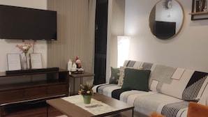 Een moderne woonkamer met een flatscreen televisie, een bank, een bijzettafeltje en een decoratieve plant.
