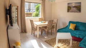 A living room with a teal sofa, a white coffee table, a dining table with patterned chairs, and a painting on the wall. -  1 bedroom 1 bathroom apartment in a quiet street in the heart of Chelsea, (London)