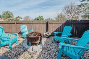 A backyard with a fire pit, four turquoise Adirondack chairs, and a wooden fence. - Millhouse: Private Pool + Dog Friendly Fenced Yard (Staunton)