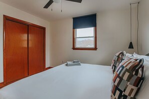 Un dormitorio con una cama grande, un armario, una ventana con persiana azul y un ventilador de techo.