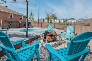 A backyard with a swimming pool, Adirondack chairs, a fire pit, and a wooden deck.
