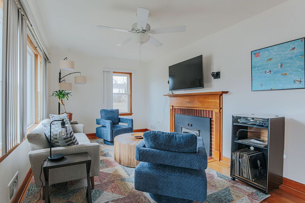 A living room with a fireplace, a flat-screen TV, a ceiling fan, and a bookshelf.