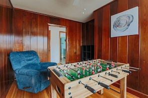 Una habitació amb un mur amb panells de fusta, un butac armchair blau i una taula de futbolí.