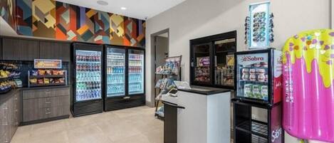 Un área comercial moderna con dispensadores refrigerados para bebidas, una exhibición de snacks y un diseño de pared colorido.