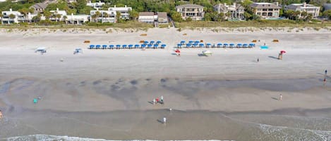 A beach with umbrellas and people, a sandy shore, and houses in the background.