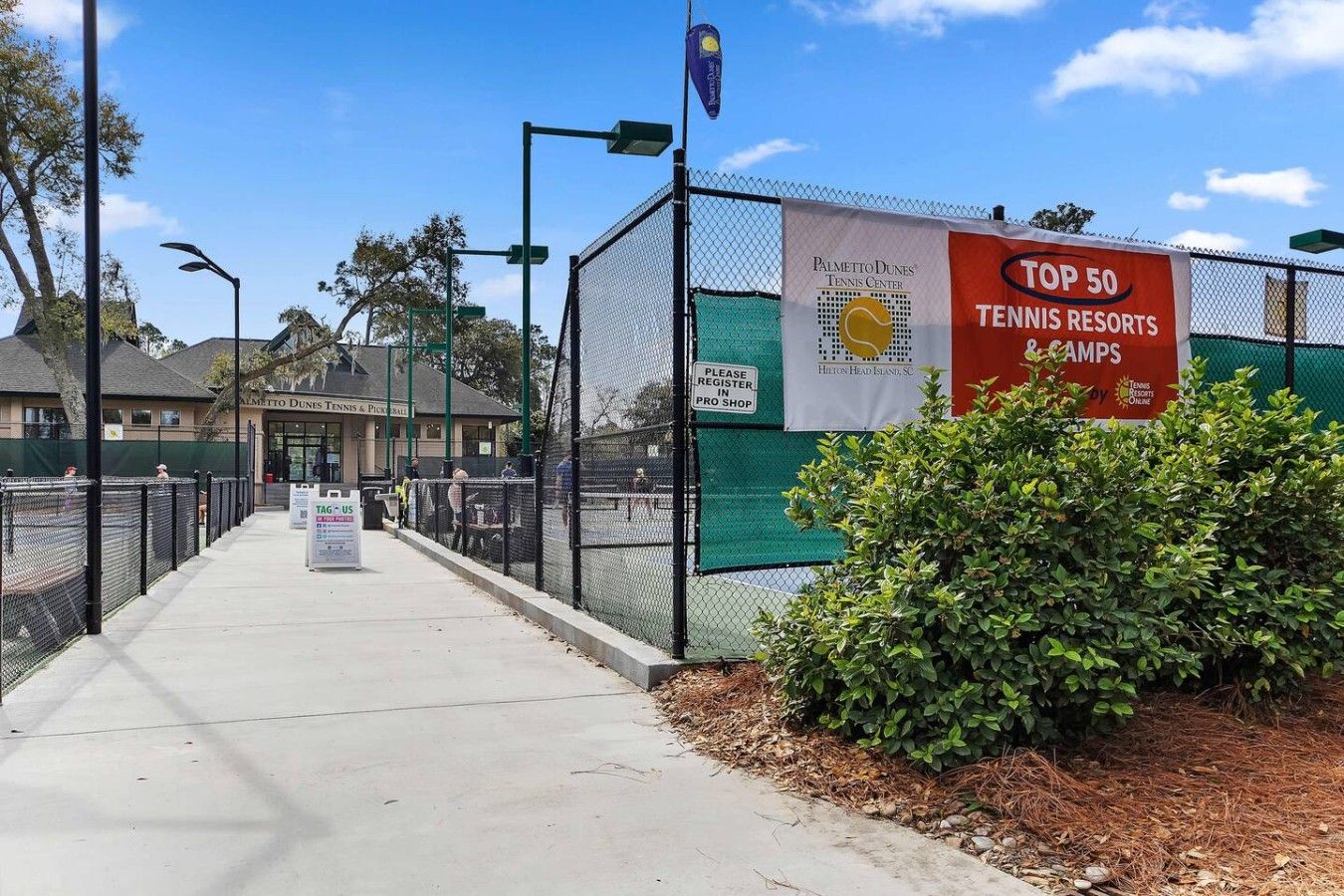 Una cancha de tenis con un cartel que anuncia 'Top 50 Tennis Resorts & Camps' y un letrero del 'Palmetto Dunes Tennis Center'.